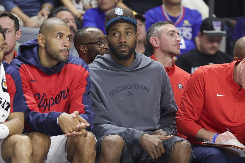 Injured Clippers forward Kawhi Leonard sits on the bench in street clothes during a preseason game.