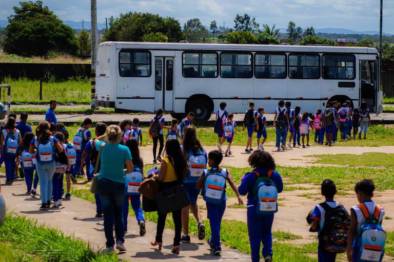 Grupo de crianças vestindo uniformes azuis caminhando em direção a um ônibus escolar