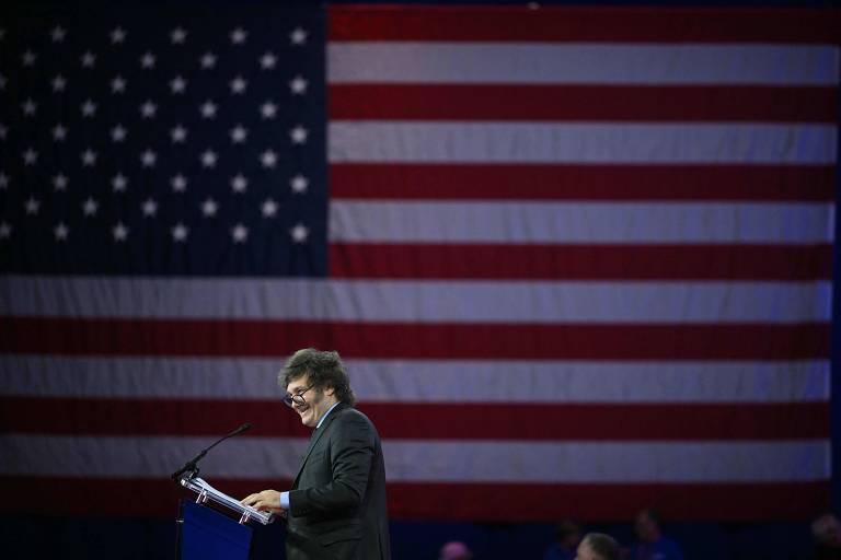 Javier Milei discursando em evento com bandeira dos EUA ao fundo