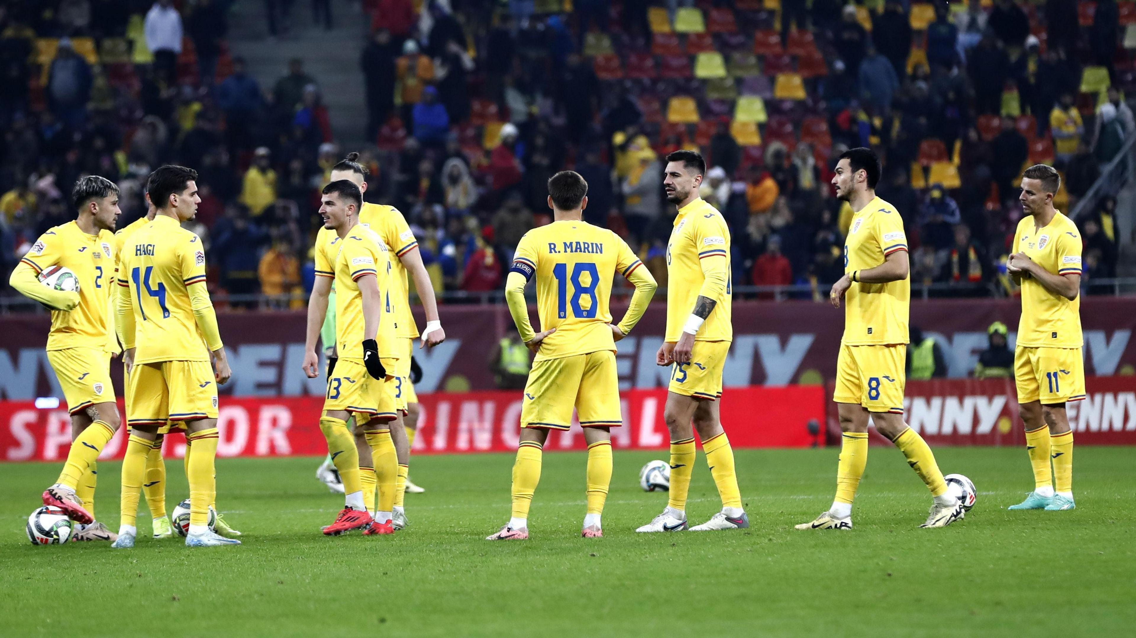 Jogadores da Romênia aguardam no campo.