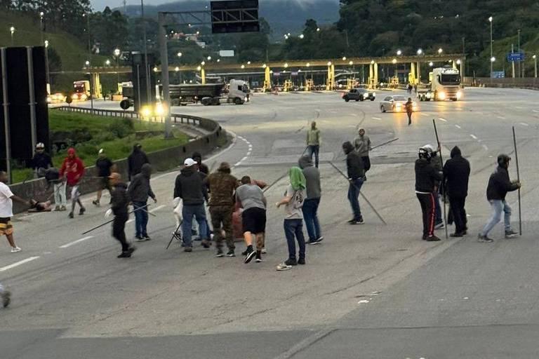 Homens com barras de ferro em uma rodovia na altura do pedágio.