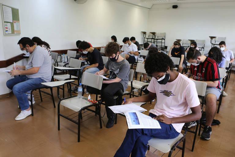 Vários alunos sentados em uma sala de aula fazendo uma prova com máscaras de proteção