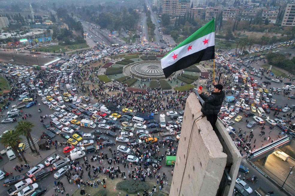 Homem ergue bandeira rebelde síria na Praça Umayyad, em Damasco, em comemoração à queda de Bashar al-Assad