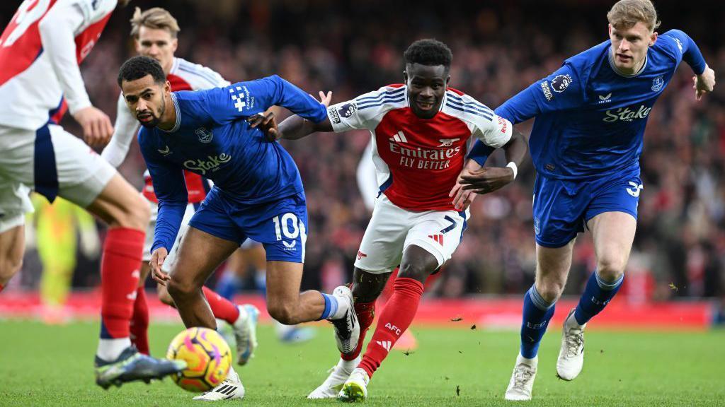 Bukayo Saka e jogadores do Everton disputando a bola.