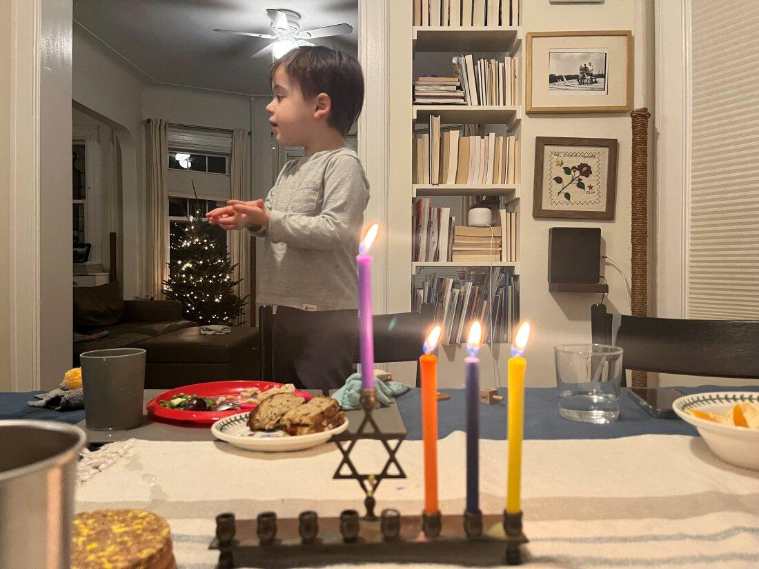 Criança entre a árvore de Natal e a menorá de Hanukkah