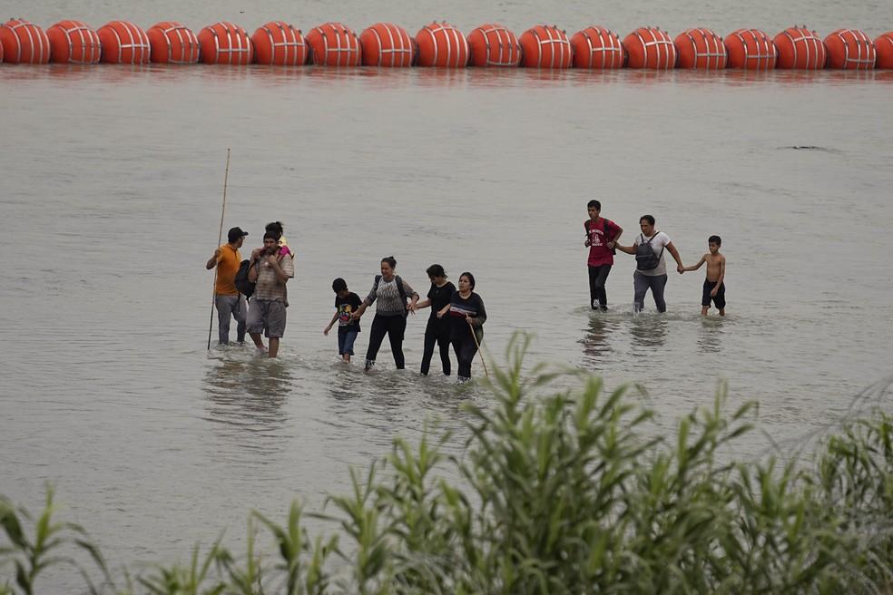 Migrantes tentam cruzar o Rio Grande, nos Estados Unidos, enquanto grandes bolas formam barreira flutuante na fronteira — Foto: Eric Gay/AP