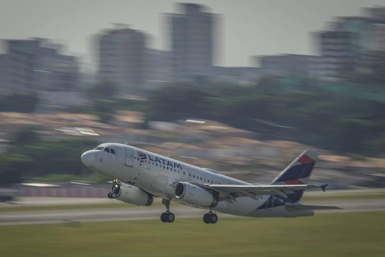 Um avião está decolando em uma pista, com a cidade ao fundo.