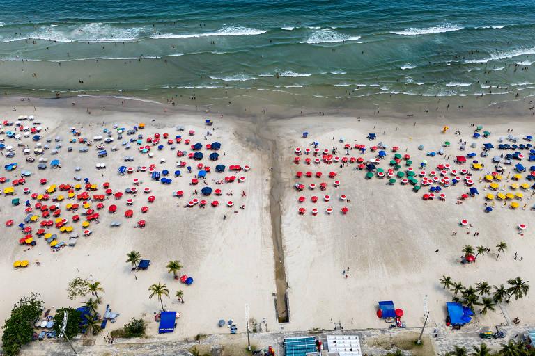 Praia movimentada em Guarujá com várias pessoas e guarda-sóis coloridos