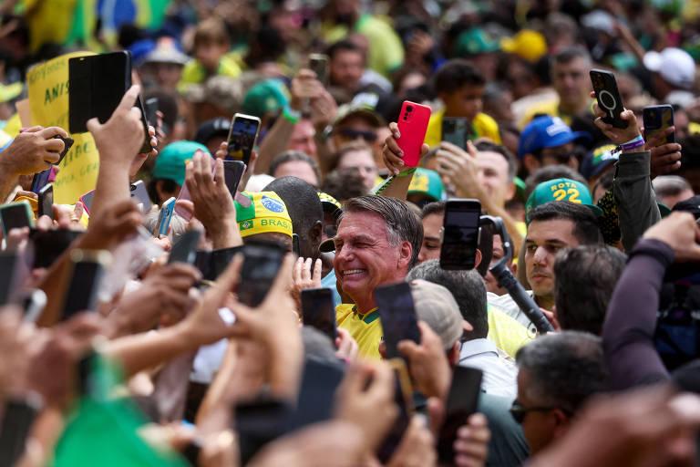 Multidão reunida em ato de Bolsonaro, com apoiadores segurando celulares e bandeiras do Brasil.