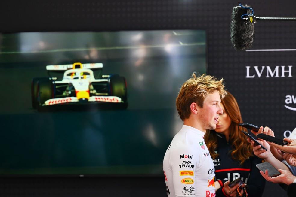 Liam Lawson dá entrevista com carro da RB na televisão ao fundo