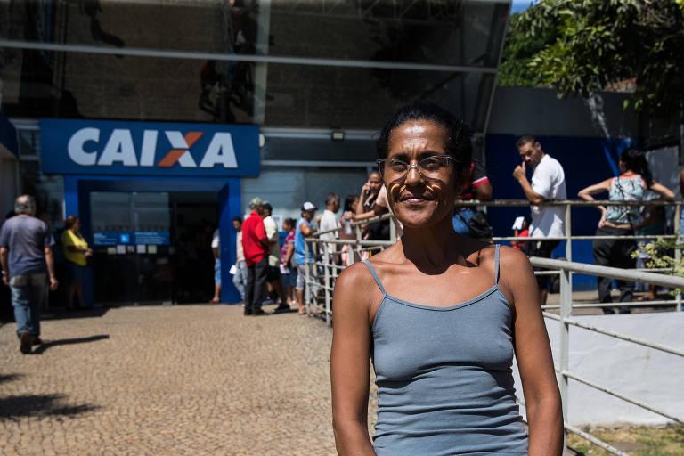 Mulher sorrindo em frente à agência da Caixa Econômica
