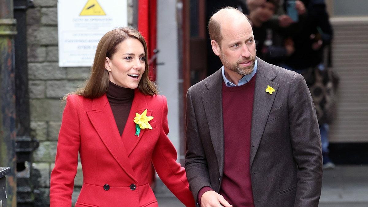 Kate Middleton em um casaco vermelho e Príncipe William em um suéter vermelho
