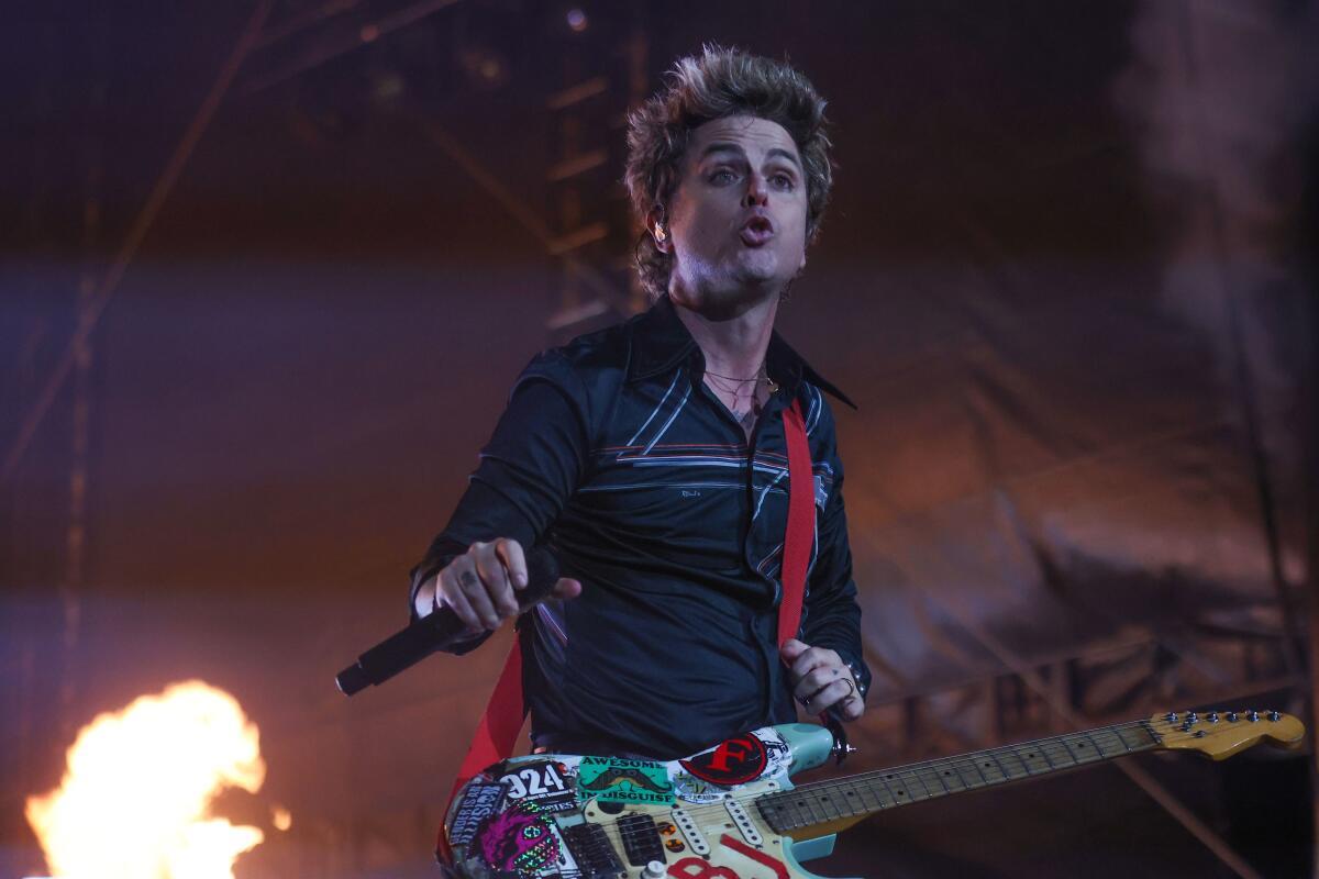 Membro da banda Green Day com guitarra e microfone próximo a chamas