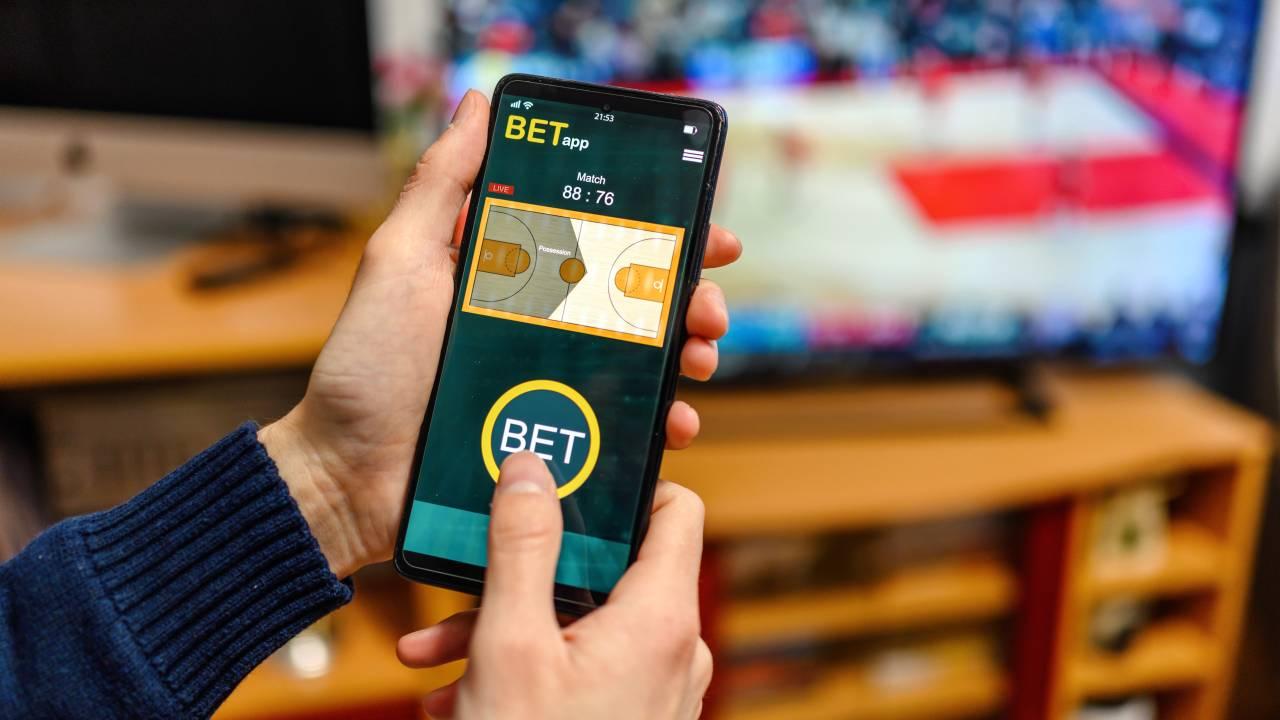 Jovens assistindo um jogo de basquete e apostando usando o smartphone.