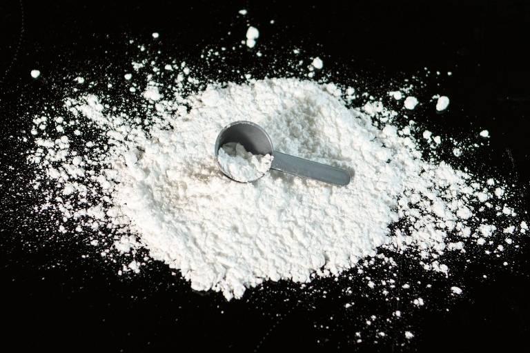 Pó branco espalhado sobre fundo preto e um pequeno dosador em cima.