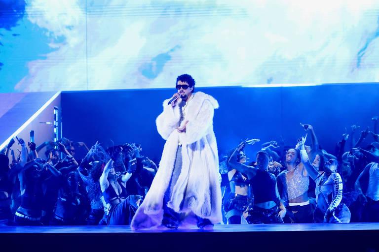 Artista se apresentando em um palco iluminado com dançarinos.