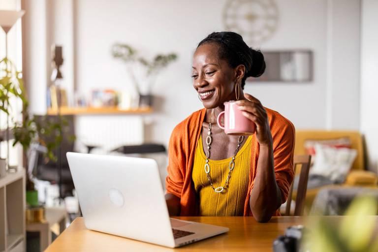 Mulher sorrindo com laptop e caneca rosa