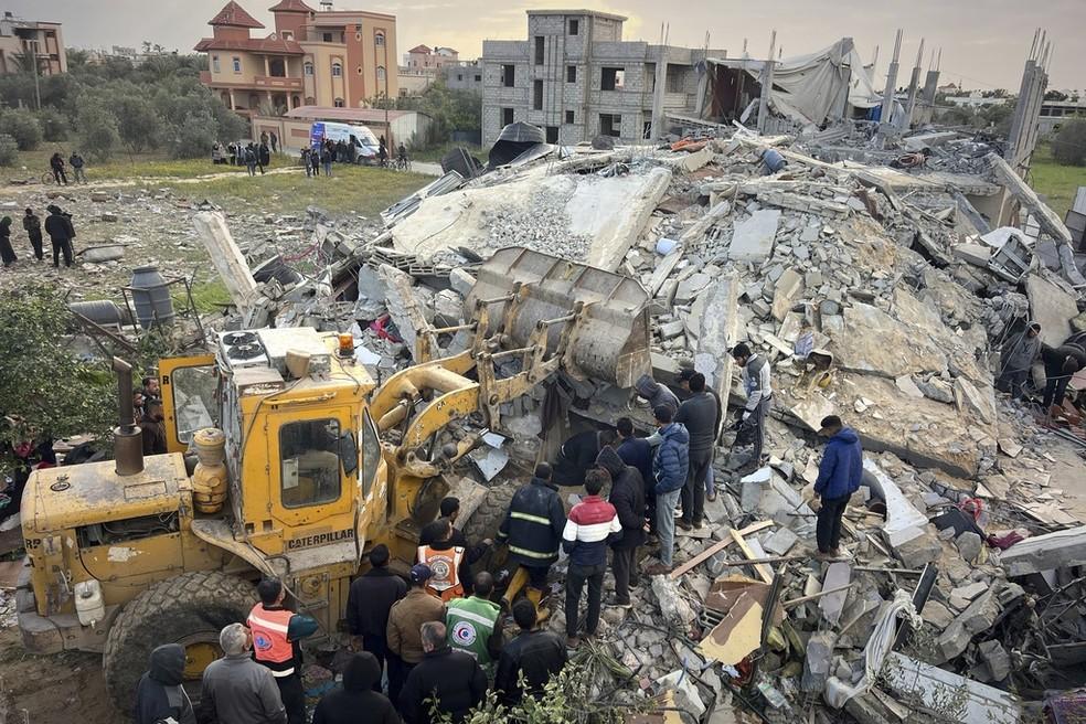 Voluntários e equipes de resgate usam uma escavadeira para remover os escombros de prédio destruído em Gaza