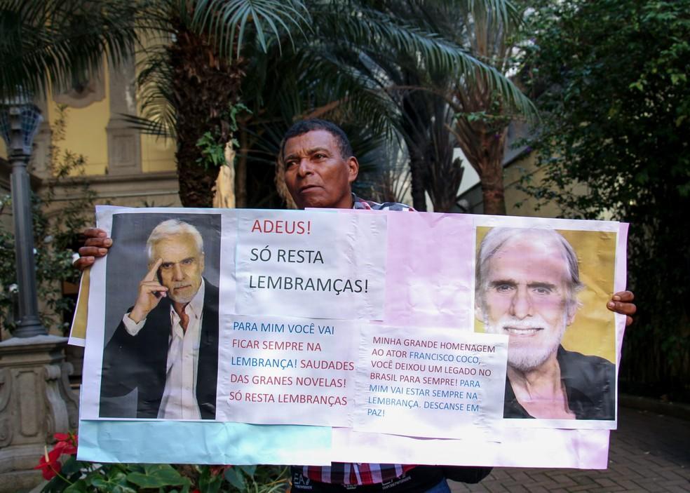 Fã segura um cartaz e faz homenagem em frente ao local