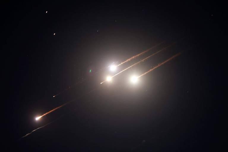 Céu noturno com feixes de luz representando mísseis em movimento