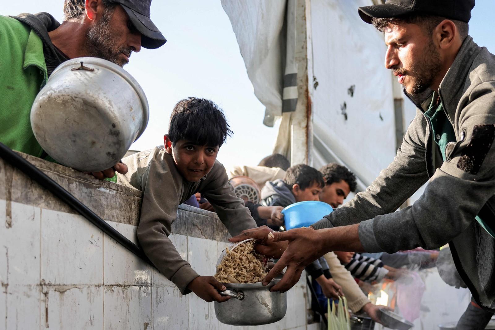 Moradores da Cidade de Gaza levam panelas para receber alimentos doados durante o mês sagrado do Ramadã