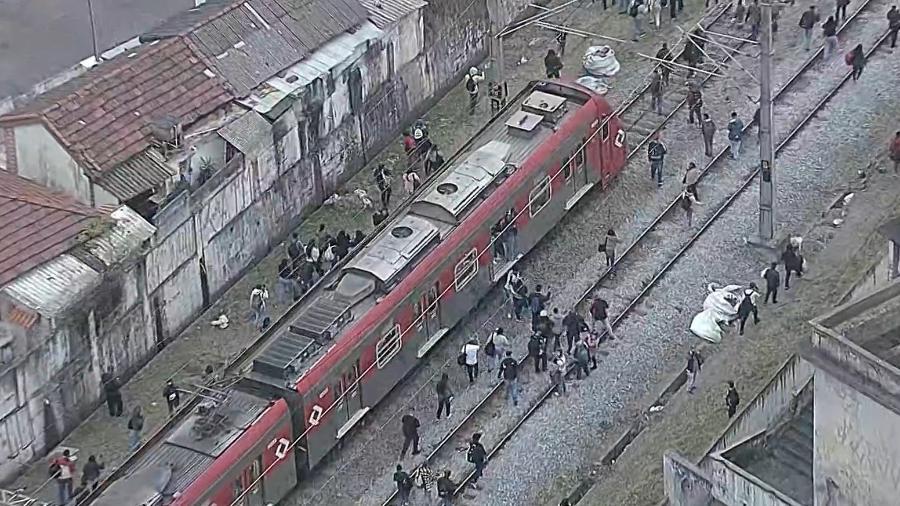 Imagens aéreas mostram passageiros descendo do trem e caminhando pelos trilhos