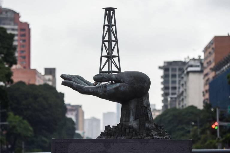 Escultura de uma mão humana em bronze que sustenta uma torre de petróleo