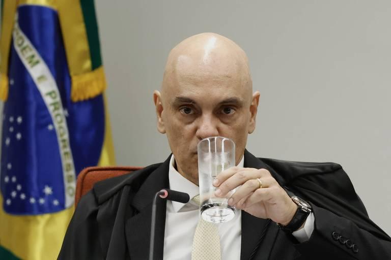 Um homem calvo, vestido com um terno escuro e uma camisa clara, observa com atenção.