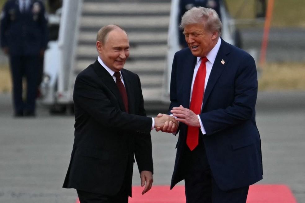 Putin e Trump rindo após se encontrarem, momento que enfatiza a cordialidade do encontro.