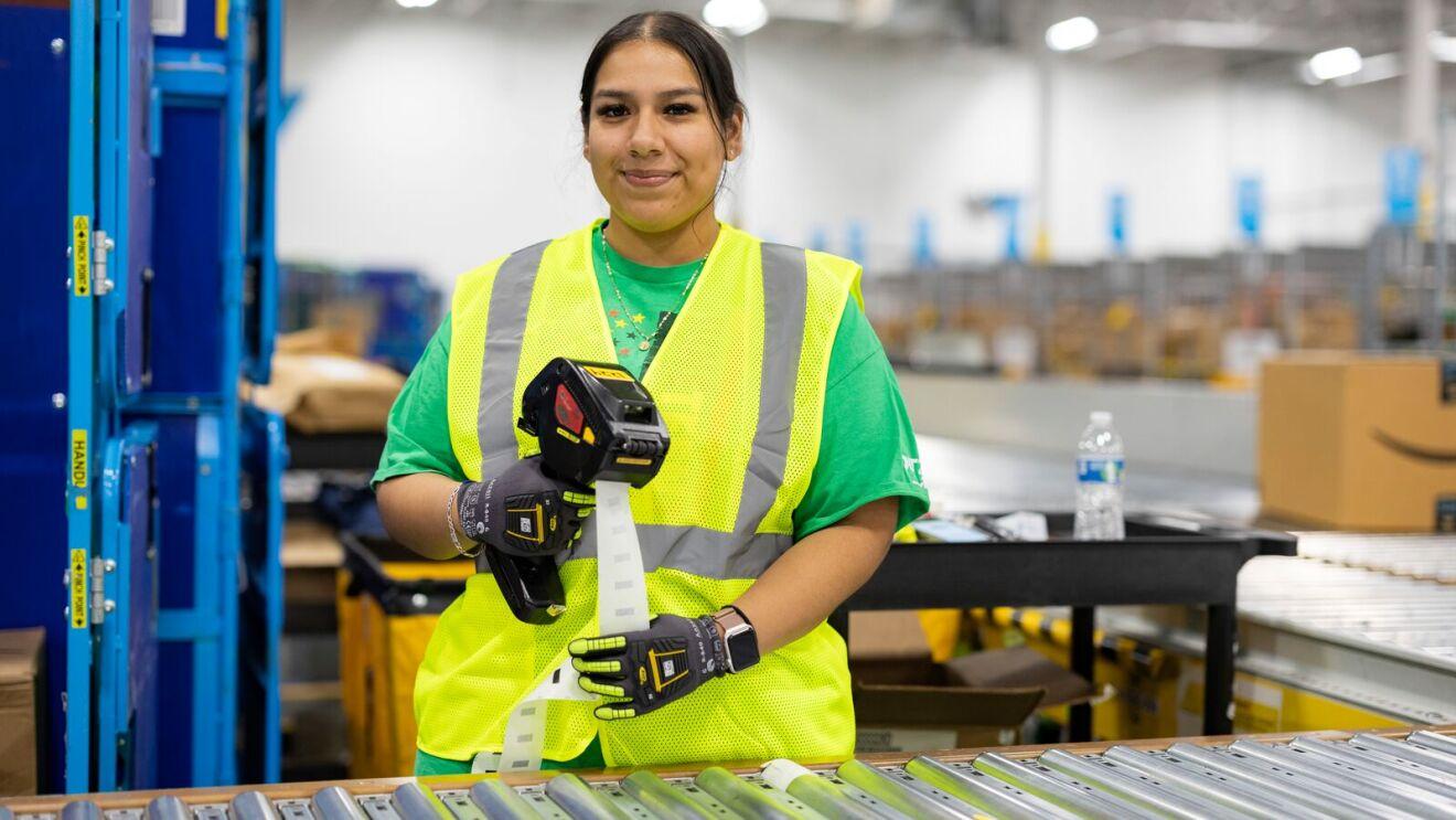 Employee in safety vest holding scanner by conveyor belt