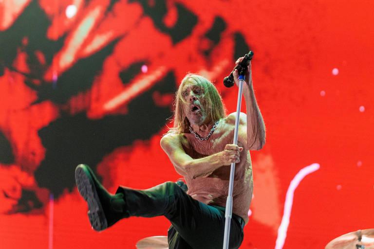 Iggy Pop se apresenta no palco, segurando um microfone com intensidade.