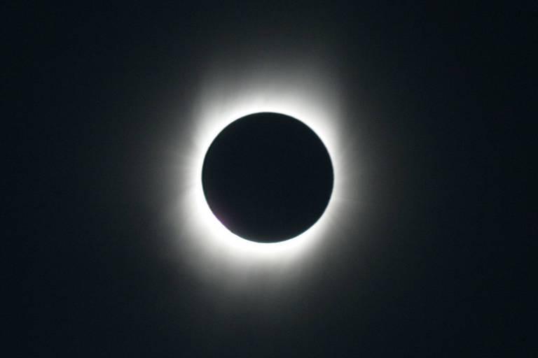 Eclipse solar total, onde a Lua cobre completamente o Sol, com uma coroa de luz visível ao redor.