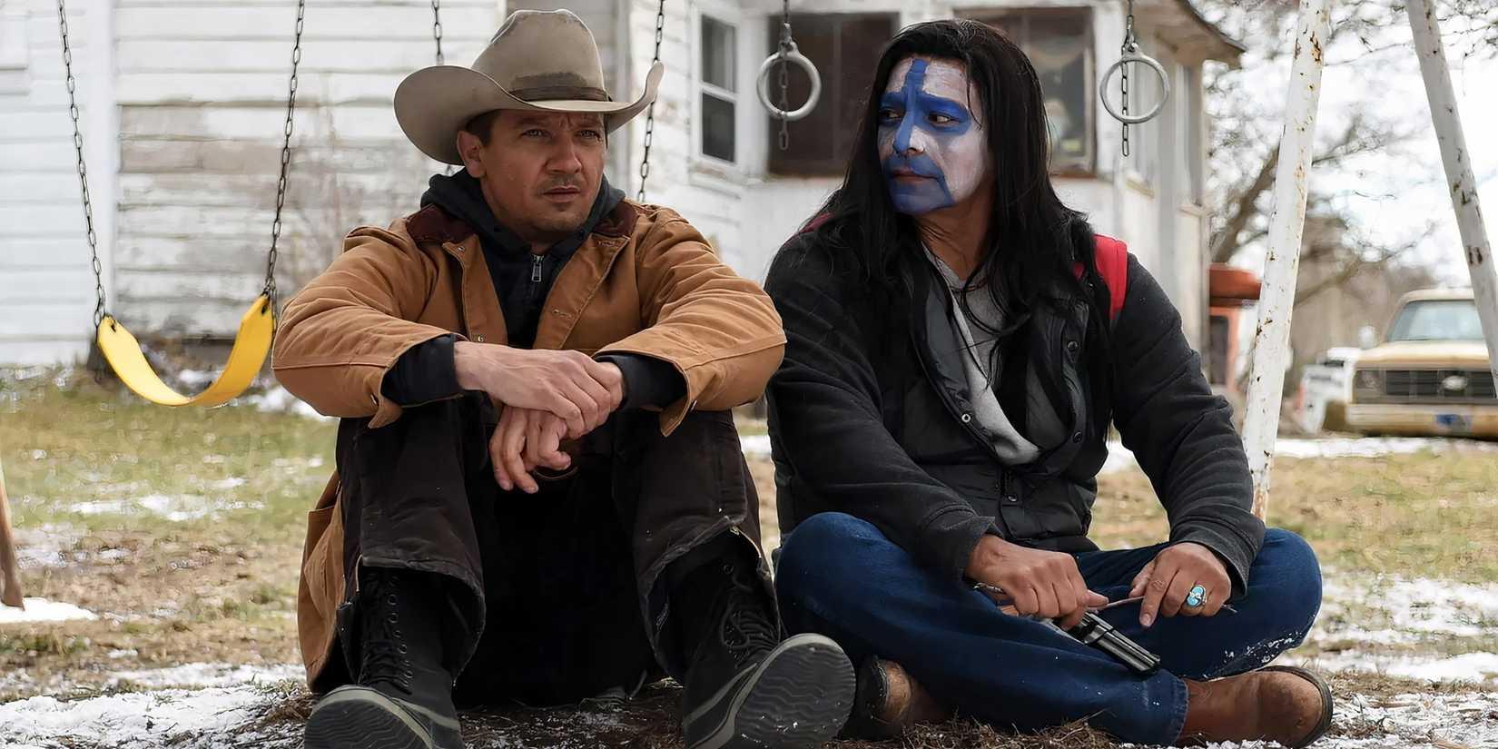 Gil Birmingham's Martin em face paint olhando para Jeremy Renner's Cory enquanto estão no chão em Wind River
