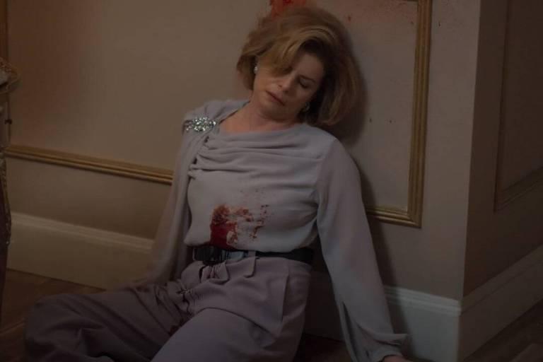 Cena com mulher de cabelos curtos e loiros sentada no chão