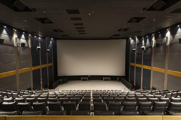 Sala de cinema com poltronas pretas vazias voltadas para uma grande tela branca