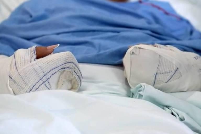 Paciente com as mãos imobilizadas em cama hospitalar