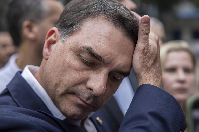 Homem de terno azul escuro ajeita o cabelo com a mão direita, com expressão séria.