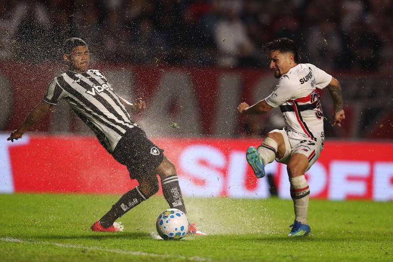 Jogadores disputam a bola em campo molhado durante jogo noturno.