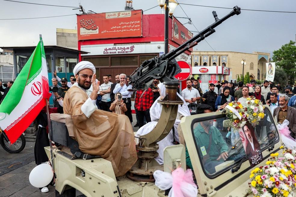 Um clérigo muçulmano xiita acena ao lado de sua noiva em um jipe militar durante a cerimônia pública de casamento coletivo na Praça Imam Hossein, em Teerã, em 18 de maio de 2026.