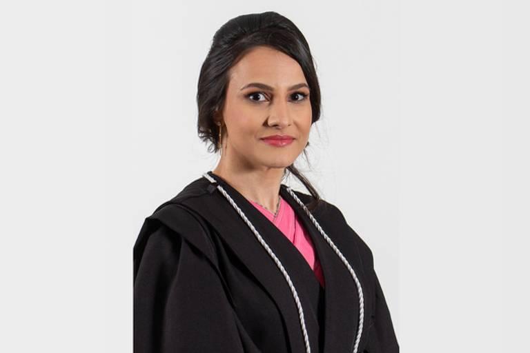 Mulher de cabelos escuros presos, veste beca preta com detalhes brancos