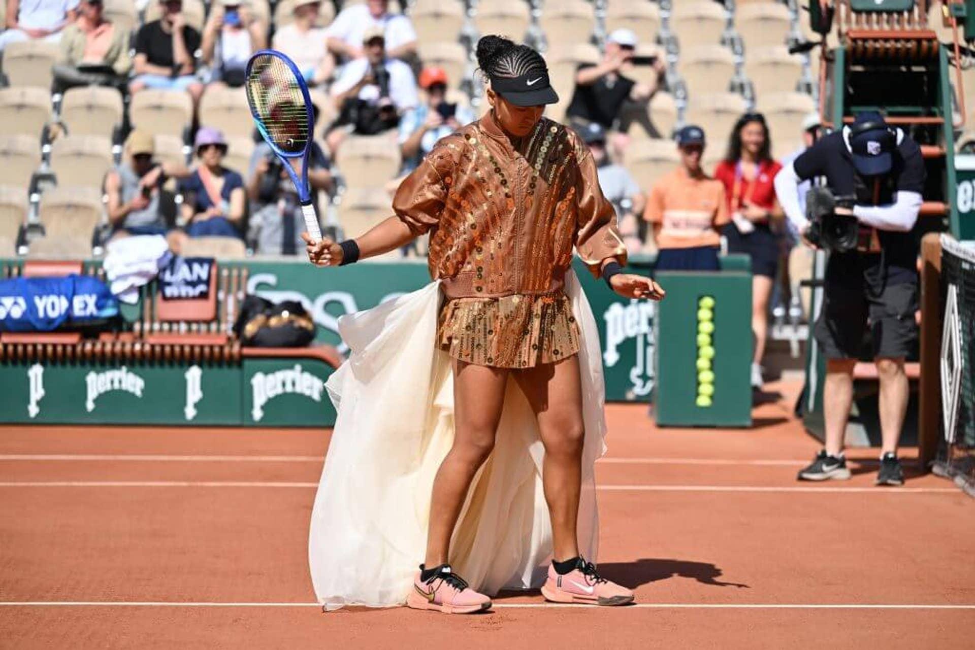 Naomi Osaka usa um vestido de tênis dourado com saia branca fluida.