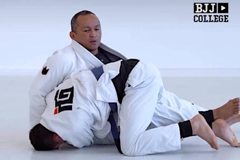 Dois praticantes de Jiu-Jitsu em kimono branco executam técnica de finalização no chão