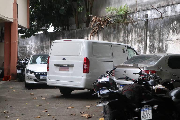 Van branca estacionada entre carros e motos em área externa