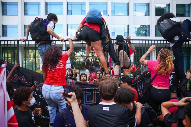 Grupo de manifestantes escalando uma grade