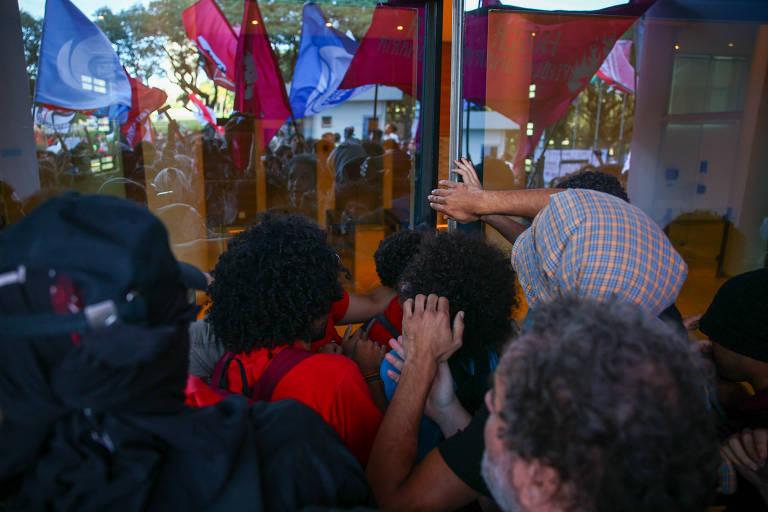 Manifestantes empurrando porta de vidro de entrada do prédio