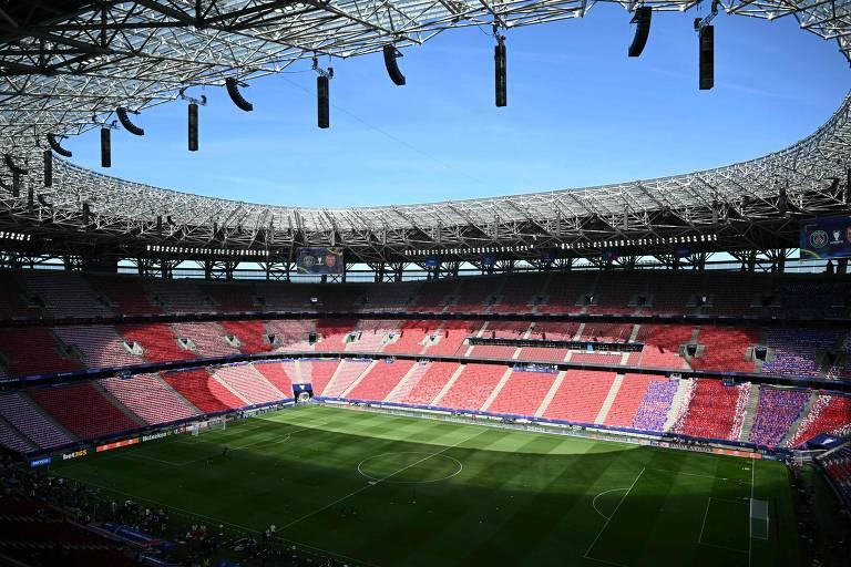 Estádio de futebol moderno com gramado verde e arquibancadas predominantemente vermelhas