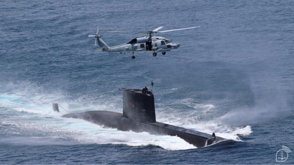 Submarino da Marinha do Brasil navega em alta velocidade no Atlântico enquanto helicóptero militar realiza operação aérea