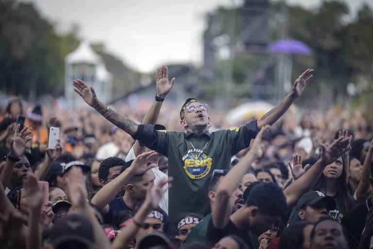 Multidão em evento ao ar livre, com pessoas demonstrando entusiasmo. Homens e mulheres estão com os braços levantados em celebração.