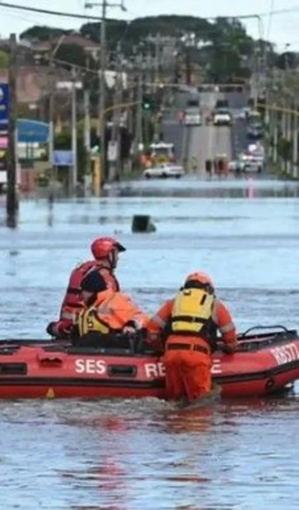 Três pessoas em um barco de resgate em local alagado.