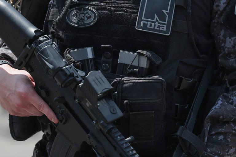 Um policial em uniforme tático escuro, segurando um fuzil.